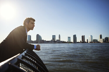 Side view of businessman standing at railing by river against clear sky - CAVF00206