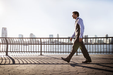 Businessman walking on walkway by river against clear sky - CAVF00210