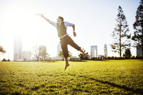 Businessman jumping and reaching plastic disk on grassy field - CAVF00214