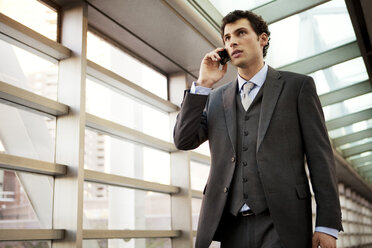 Niedriger Blickwinkel eines Geschäftsmannes, der mit seinem Handy telefoniert, während er auf einem überdachten Gehweg geht - CAVF00217