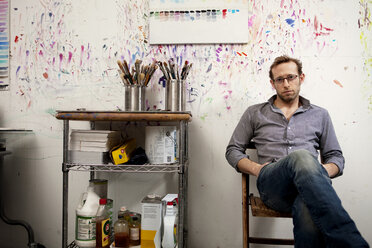 Portrait of male artist sitting on chair against wall in workshop - CAVF00269