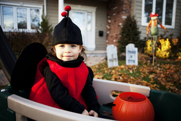 Portrait of happy girl wearing costume and sitting in cart - CAVF00279