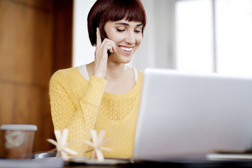 Glückliche Geschäftsfrau, die am Telefon spricht, während sie einen Laptop im Büro benutzt - CAVF00310