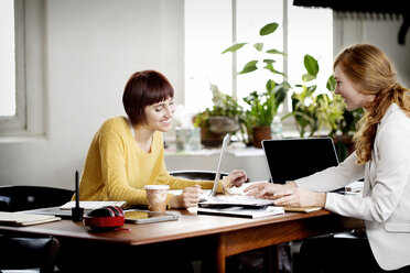 Female photo editors discussing at desk in creative office - CAVF00315