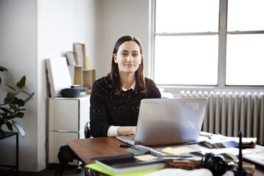 Portrait of young businesswoman working on laptop in creative office - CAVF00353