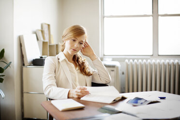 Female reading book while sitting at desk in office - CAVF00361