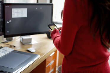 Midsection of businesswoman using phone at computer desk - CAVF00393