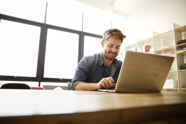 Glücklicher Mann mit Laptop am Tisch - CAVF00395