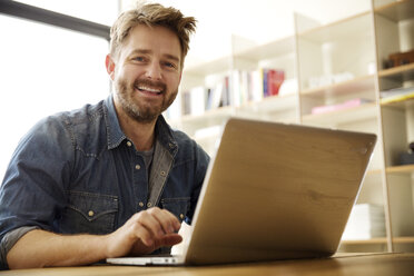 Porträt eines glücklichen Mannes, der zu Hause einen Laptop benutzt - CAVF00406