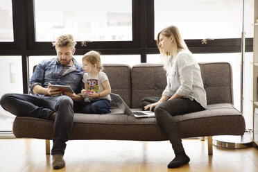 Family using technologies while sitting on sofa at home - CAVF00411