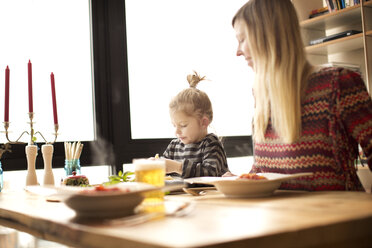 Mother looking at girl having food at table - CAVF00422