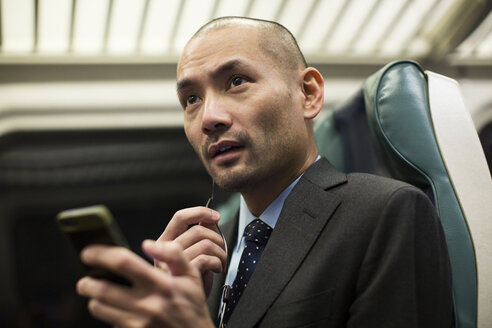 Geschäftsmann hält Smartphone während der Fahrt im Zug - CAVF00426