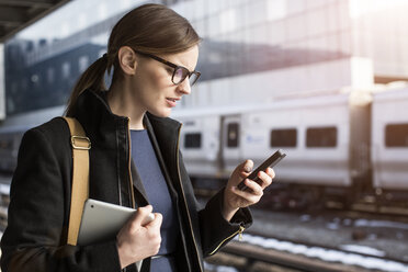 Junge Geschäftsfrau schreibt Textnachrichten, während sie am Bahnhof steht - CAVF00428