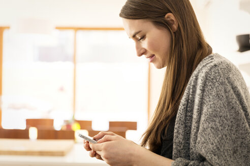 Seitenansicht einer Frau, die im Stehen zu Hause eine SMS schreibt - CAVF00450