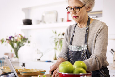 Senior woman slicing apples at table in kitchen - CAVF00466