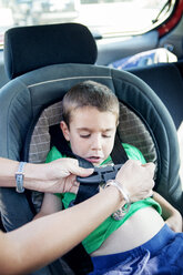 Cropped image of mother fastening seat belt of son's car seat - CAVF00482