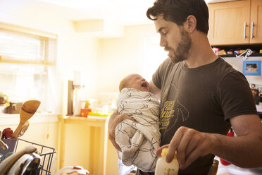 Father holding crying baby daughter in kitchen at home - CAVF00487