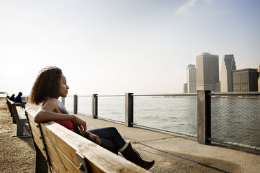 Seitenansicht einer nachdenklichen Frau, die am East River in der Stadt gegen den Himmel sitzt - CAVF00536