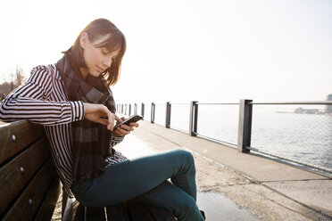 Woman using phone while sitting on bench - CAVF00538