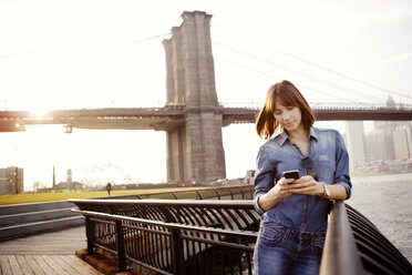 Frau schreibt SMS, während sie am Geländer der Brooklyn Bridge steht - CAVF00540