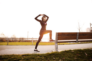 Jogger stretching by bench in park against clear sky - CAVF00553