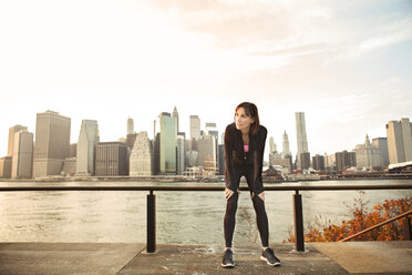 Tired woman bending by river against cityscape - CAVF00554