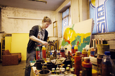 Junger männlicher Künstler malt am Tisch stehend in einem Workshop - CAVF00558