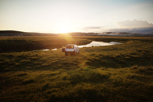 Auf einem Feld am Fluss geparktes Auto bei Sonnenuntergang - CAVF00577