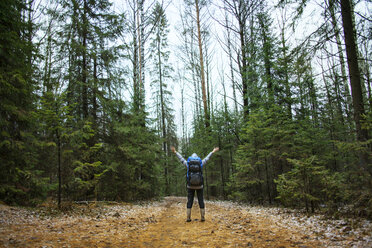 Rear view woman with arms outstretched carrying backpack in forest - CAVF00584