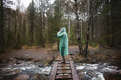 Mann mit Regenmantel auf einem Steg im Wald stehend - CAVF00590