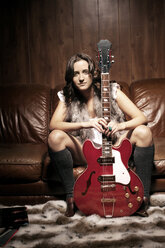Porträt einer jungen Frau mit Gitarre auf dem Sofa sitzend - CAVF00602