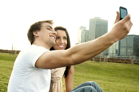 Glückliches Paar nimmt Selfie auf Rasen in der Stadt, lizenzfreies Stockfoto