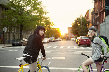 Porträt von Freunden mit Fahrrädern auf einer Straße in der Stadt bei Sonnenuntergang - CAVF00626