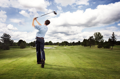 Volle Länge Rückansicht von Mann schwingt Golfschläger auf Feld gegen bewölkten Himmel, lizenzfreies Stockfoto