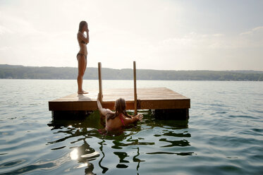 Freunde auf schwimmender Plattform im See gegen den Himmel an einem sonnigen Tag - CAVF00684