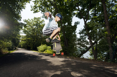 Jugendlicher führt Stunt mit Skateboard über Straße gegen Bäume aus - CAVF00692