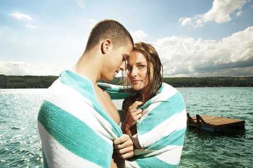 Romantic couple wrapped in towel against lake - CAVF00698