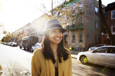 Fröhliche junge Frau mit Hut und Blick in die Ferne in der Stadt - CAVF00717