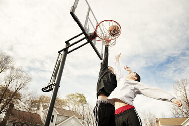 Low angle view of boys playing basketball while jumping against sky - CAVF00726