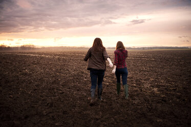 Rückansicht von Freundinnen, die bei Sonnenaufgang auf einem Feld gegen den Himmel laufen - CAVF00730