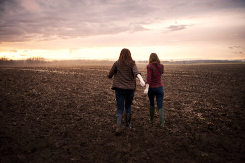 Rückansicht von Freundinnen, die bei Sonnenaufgang auf einem Feld gegen den Himmel laufen - CAVF00730