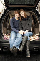 Porträt eines glücklichen jungen Paares, das im Kofferraum eines Autos sitzt - CAVF00745