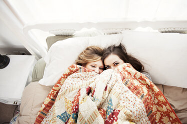 Draufsicht auf Freundinnen, die zu Hause auf dem Bett liegend durch die Decke pinkeln - CAVF00763