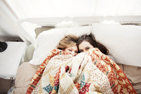 Overhead view of female friends pepping through blanket while lying on bed at home - CAVF00763