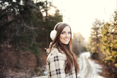 Happy woman wearing ear muff while standing on footpath during winter - CAVF00764