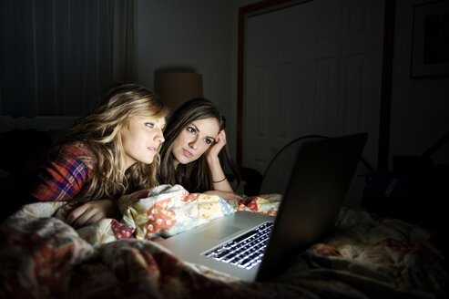 Friends using laptop while lying on bed at home - CAVF00767