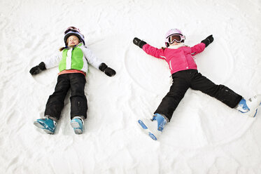 Siblings making snow angel on field during winter - CAVF00773