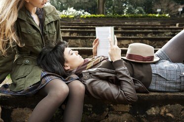 Woman reading book while lying on friends lap in park - CAVF00781