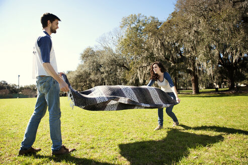 Ein Paar breitet eine Decke auf einer Wiese in einem Park aus - CAVF00783