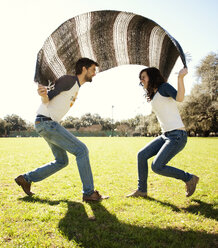 Couple playing under blanket in park during sunny day - CAVF00784